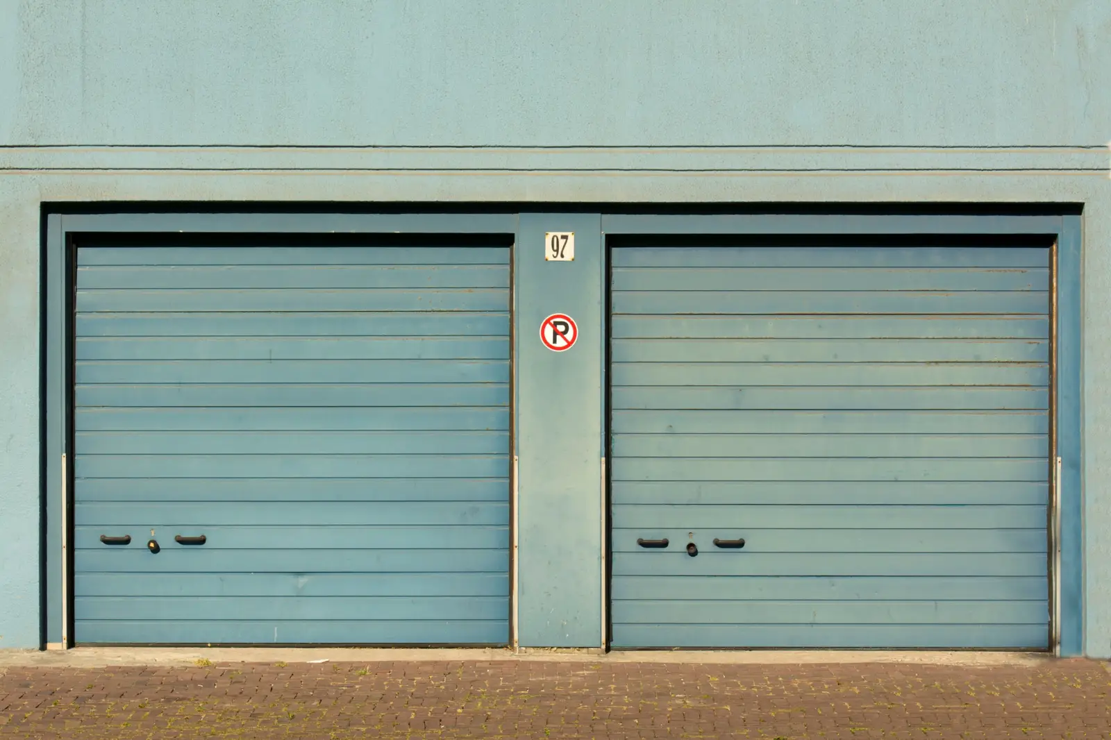 Two blue overhead doors on a commercial building with a no-parking sign between them